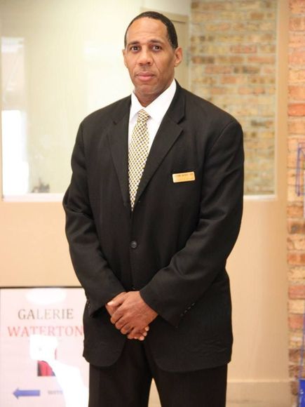 A man in a suit and tie stands in front of a brick wall