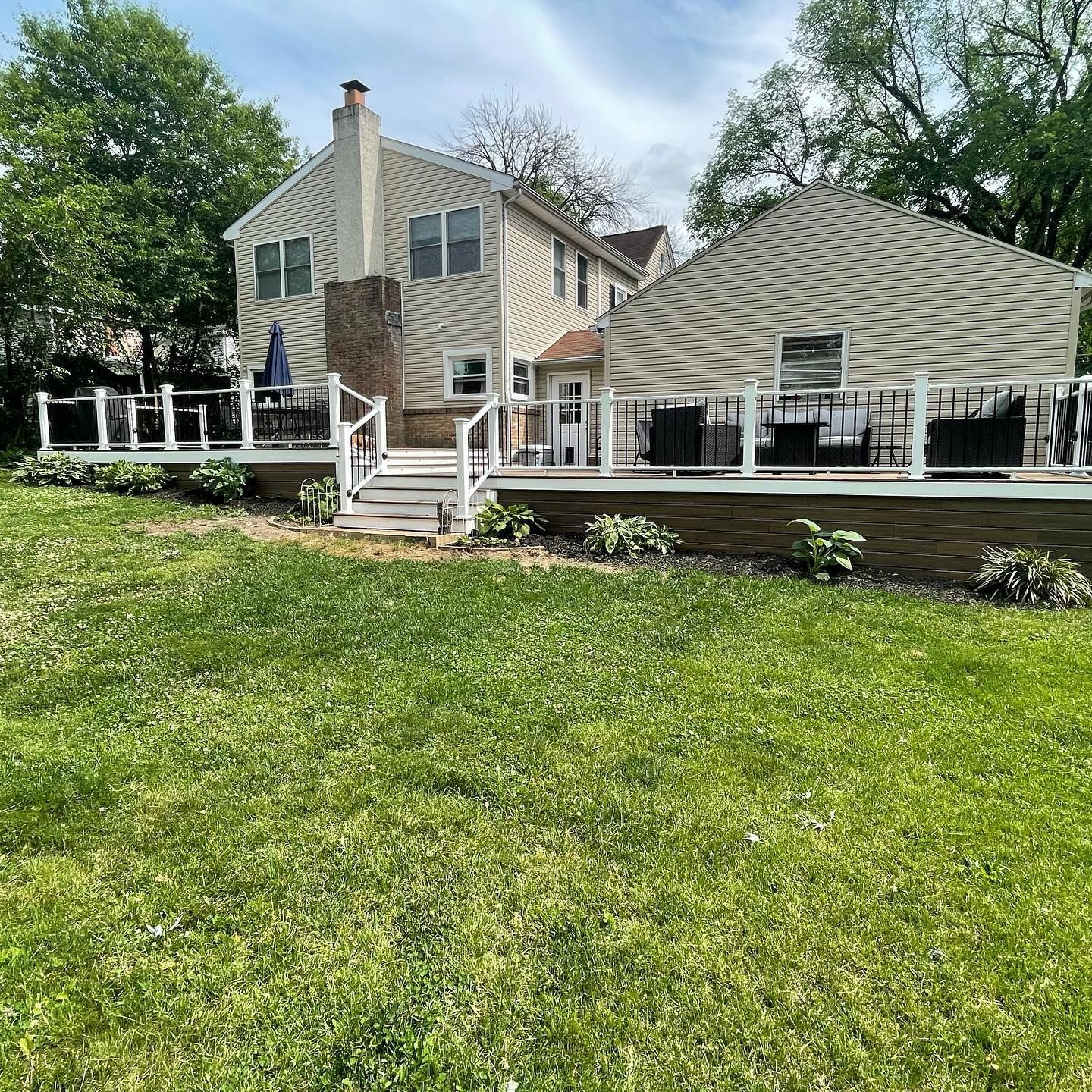 Backyard with two-story house, wooden deck, green lawn, white railing.