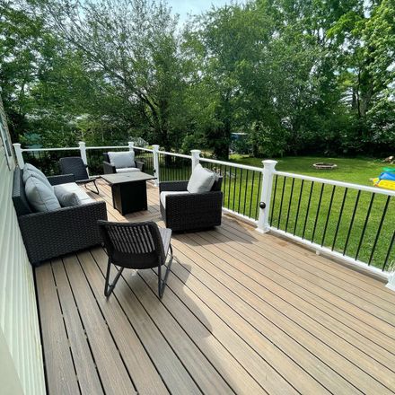 Outdoor deck with seating, green lawn, trees, and black railing.