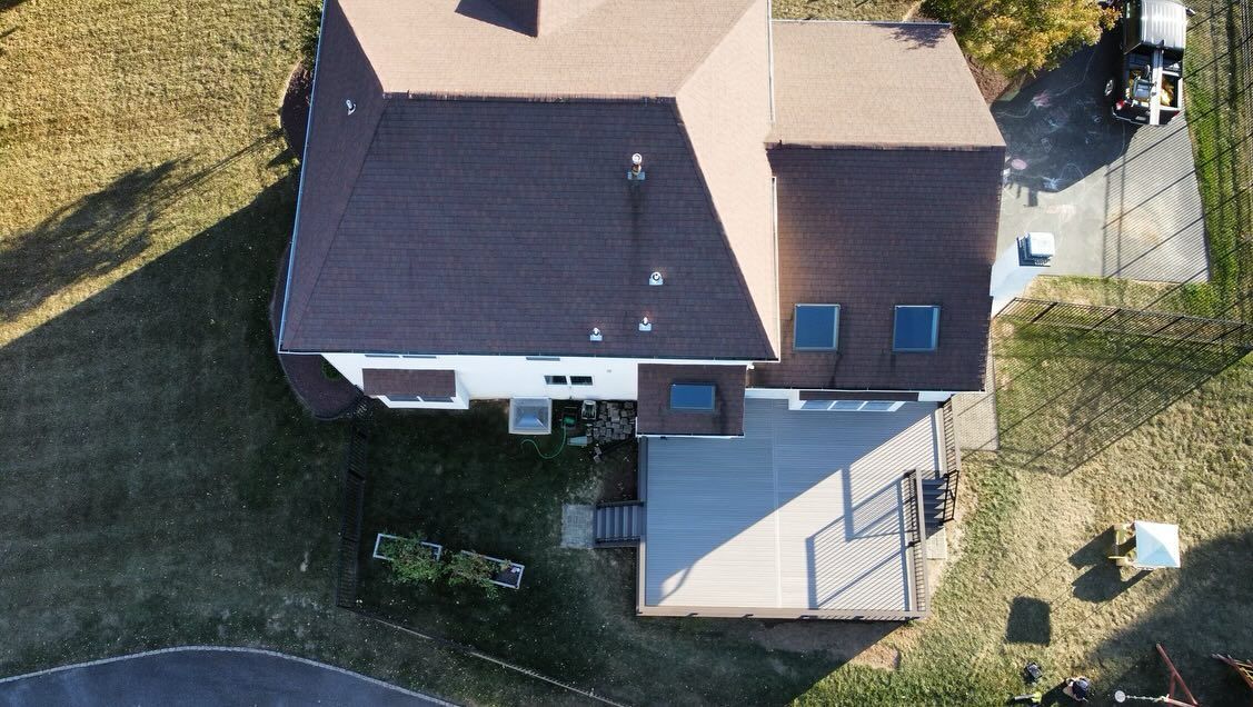 Overhead view of a two-story house with a brown roof and a gray deck. The house has a driveway and grassy yard.