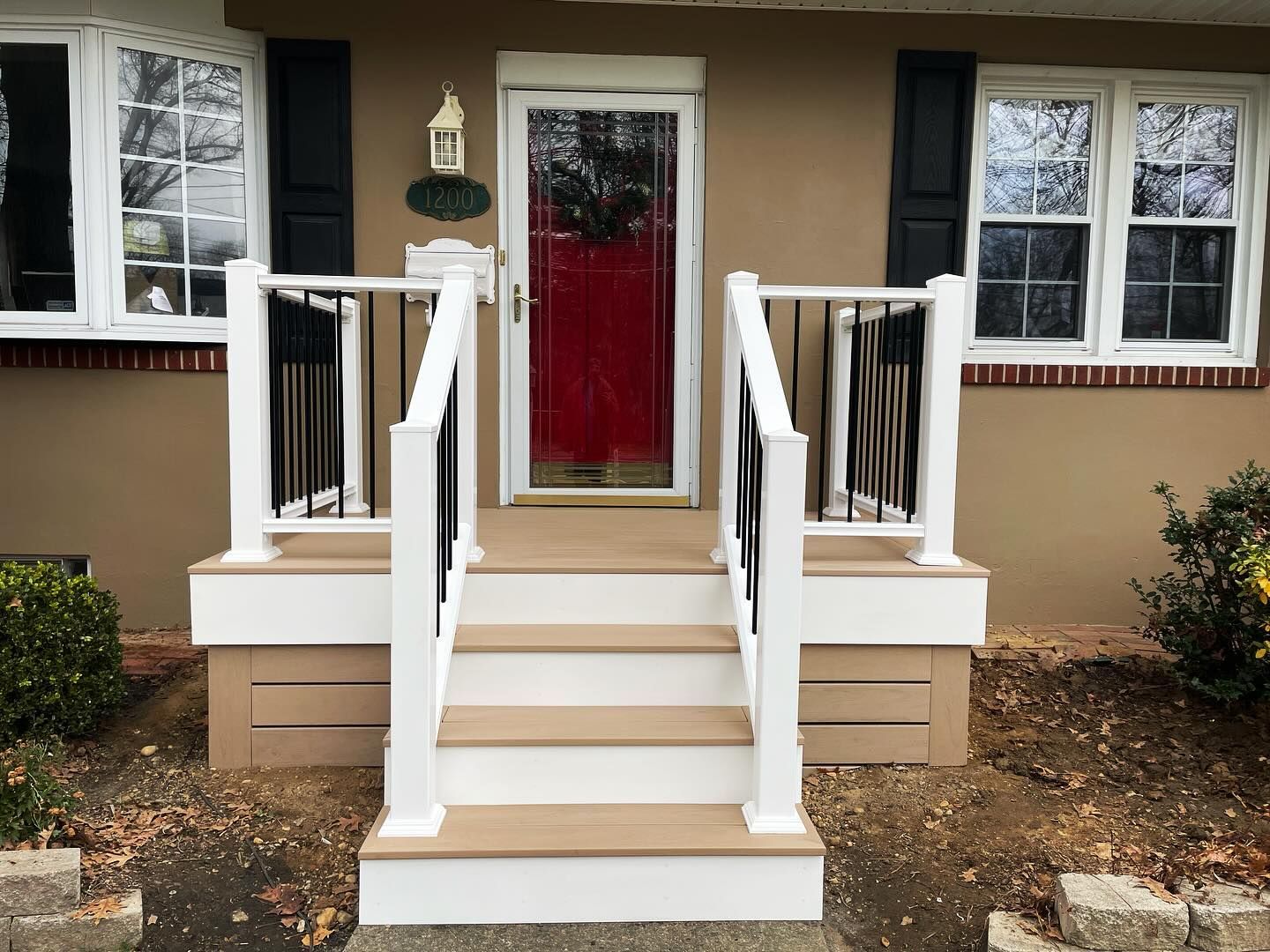 Exterior of a home with a red door, white railing, and steps.