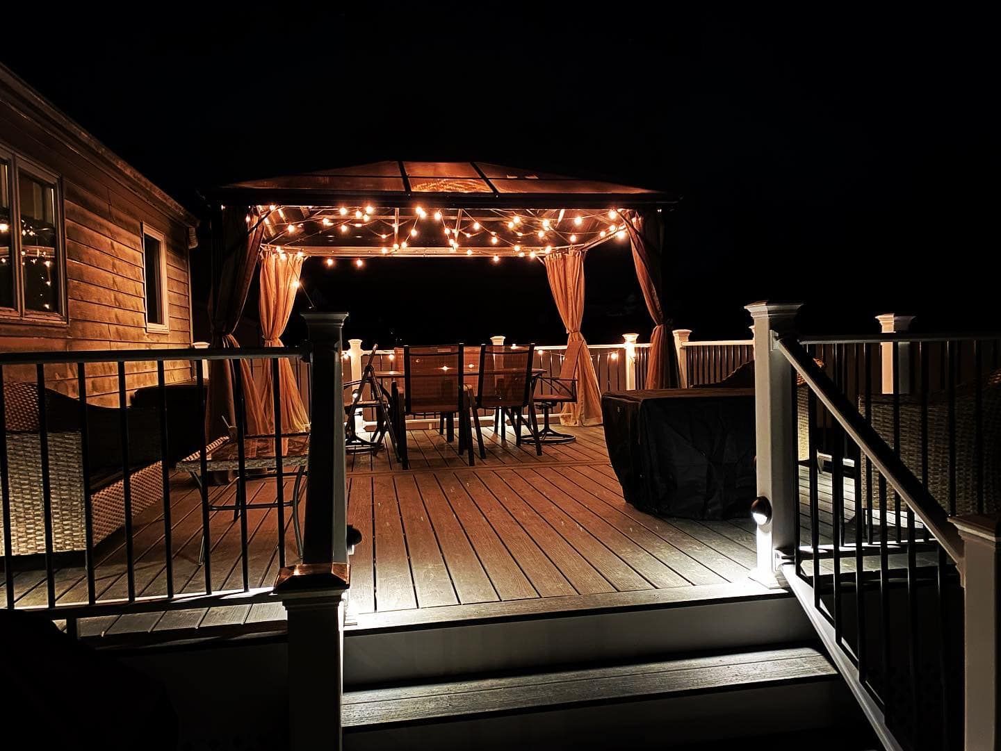 Nighttime deck with string lights around a gazebo. Chairs and table are inside the gazebo.