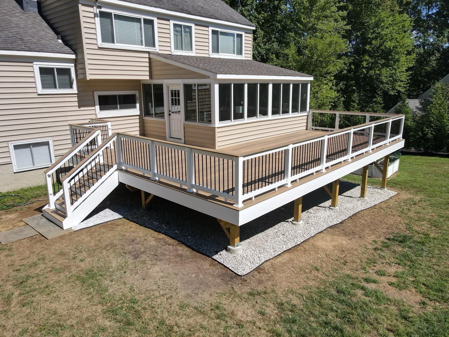A two-story house with a wooden deck and screened porch. Deck has white railings and stairs.