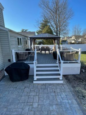 Deck with gazebo and patio. Gray and white deck with black grill cover. Sunny day.