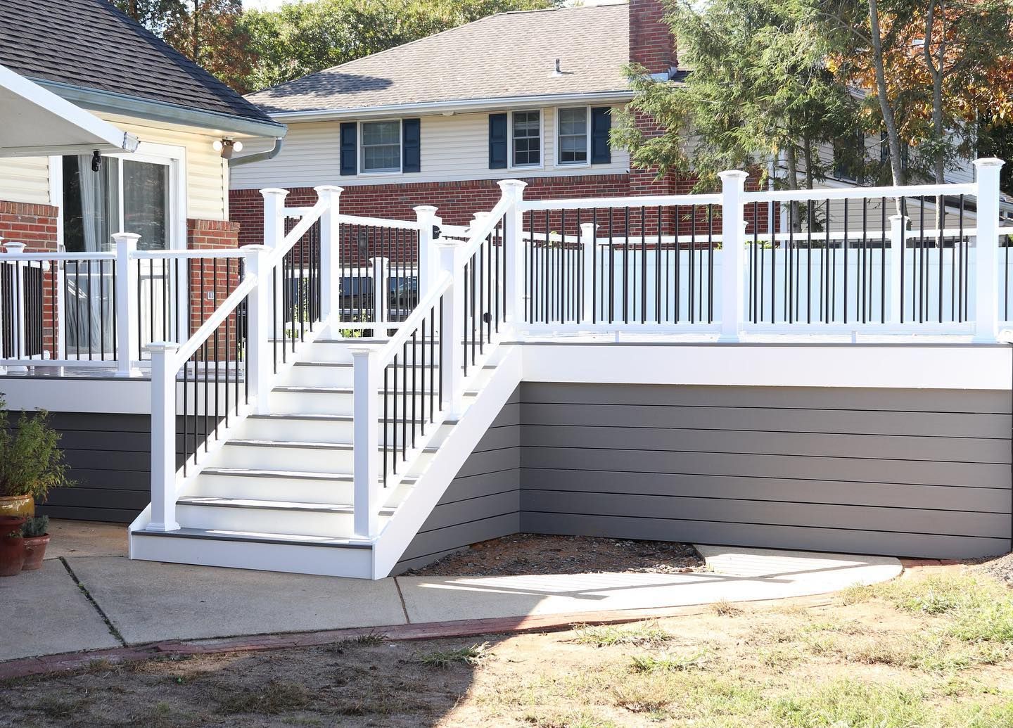 White and black deck with stairs leading to a backyard, set against two-story houses.