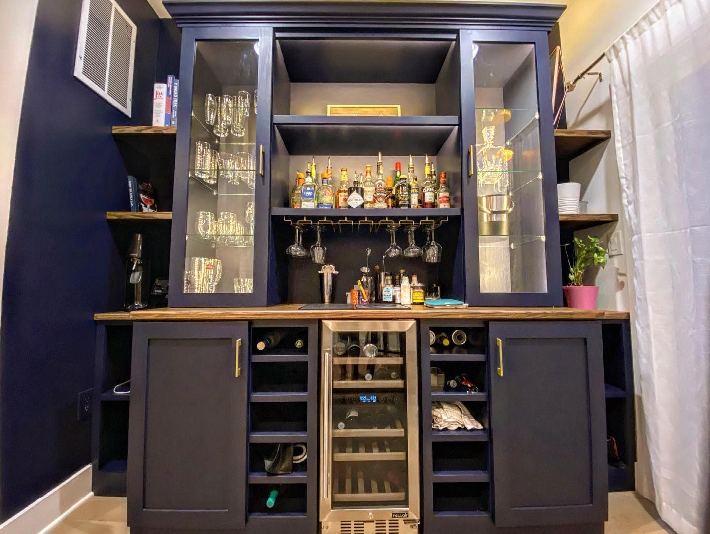 Navy blue home bar with glass-front cabinets, wine rack, and shelves, on a dark wooden countertop.
