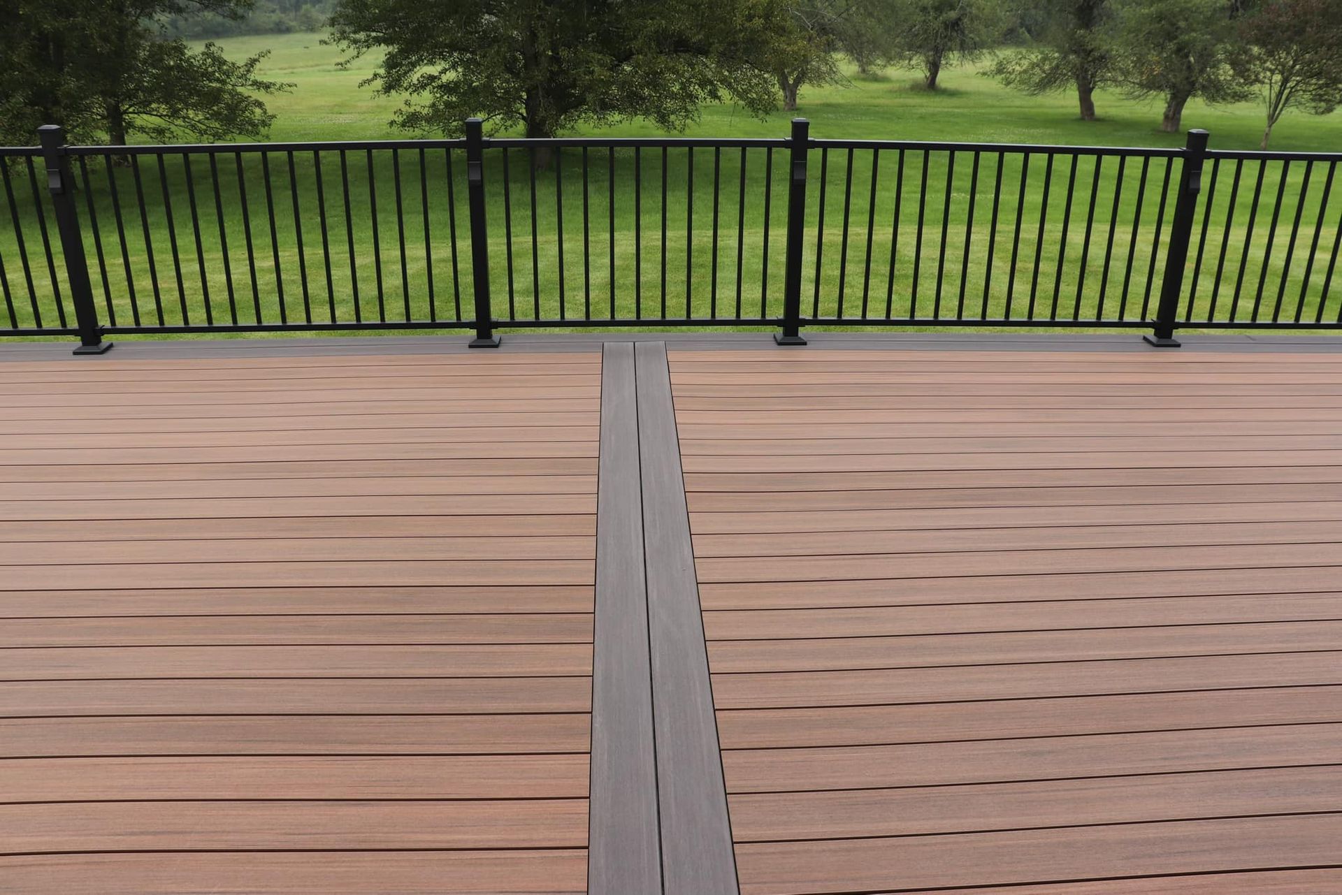 Wooden deck with black railing overlooking a green field.