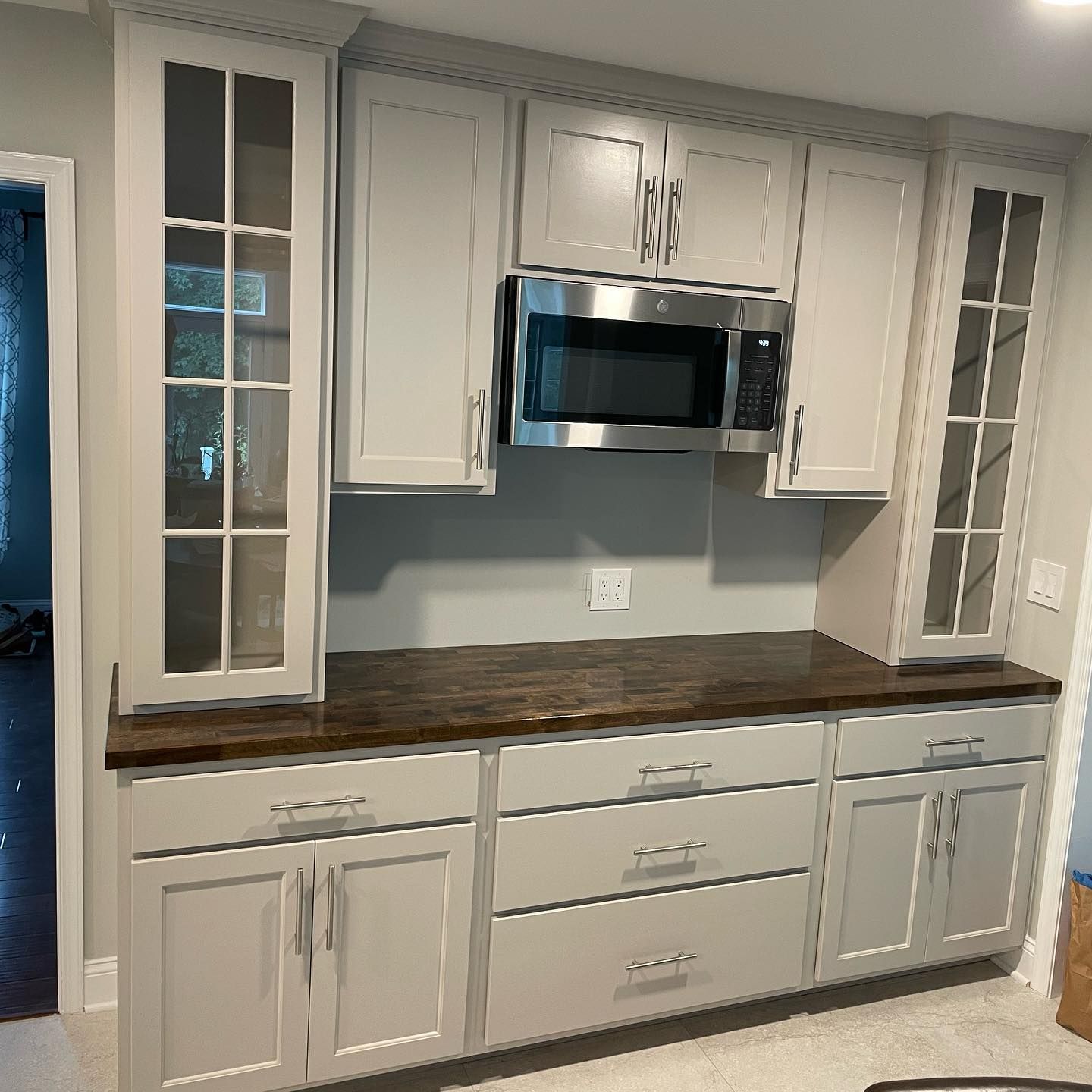 Gray kitchen cabinets with a microwave, dark countertop, and glass-paneled doors.