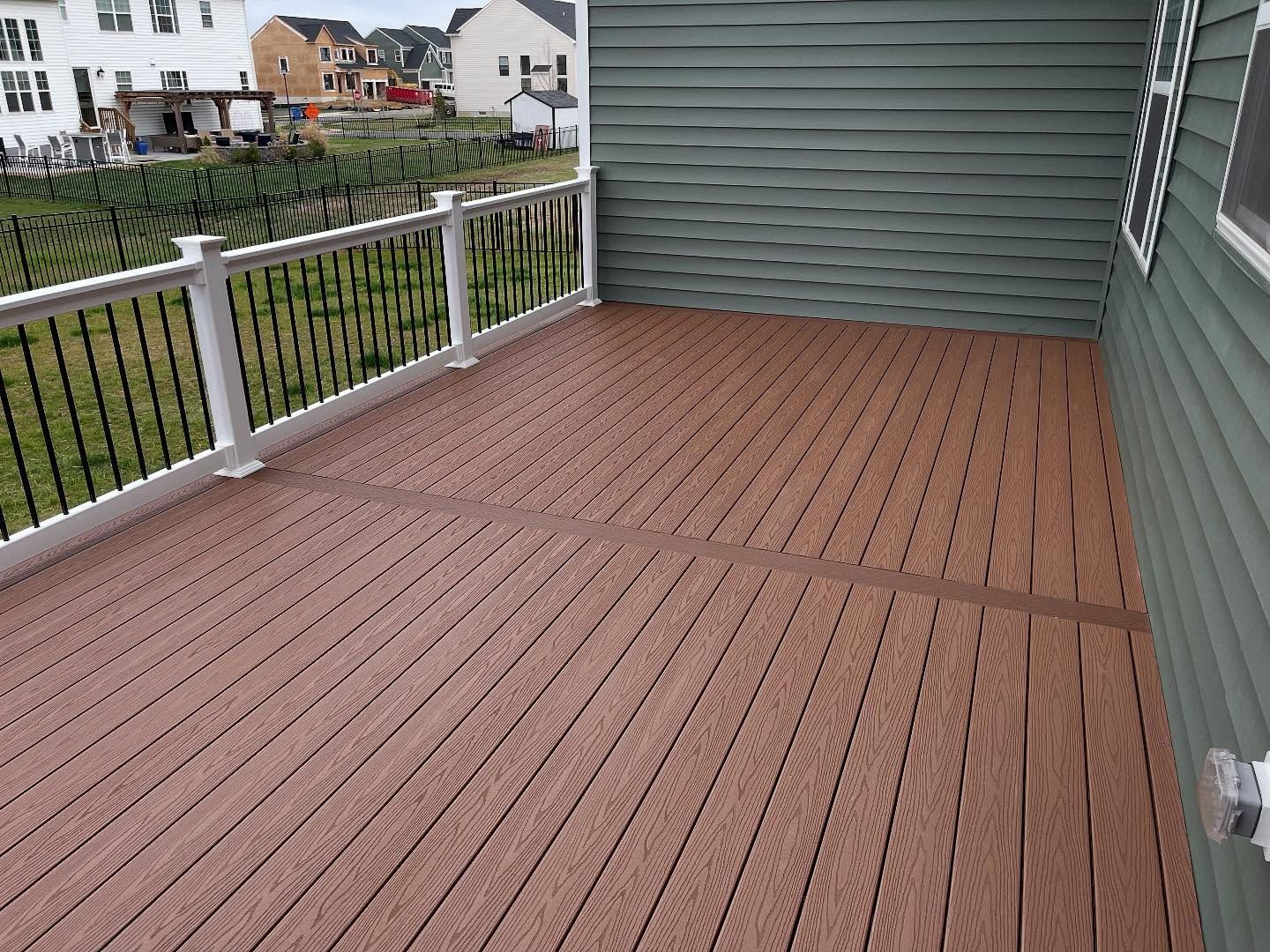 Brown composite deck with white railing, and green siding on a house.