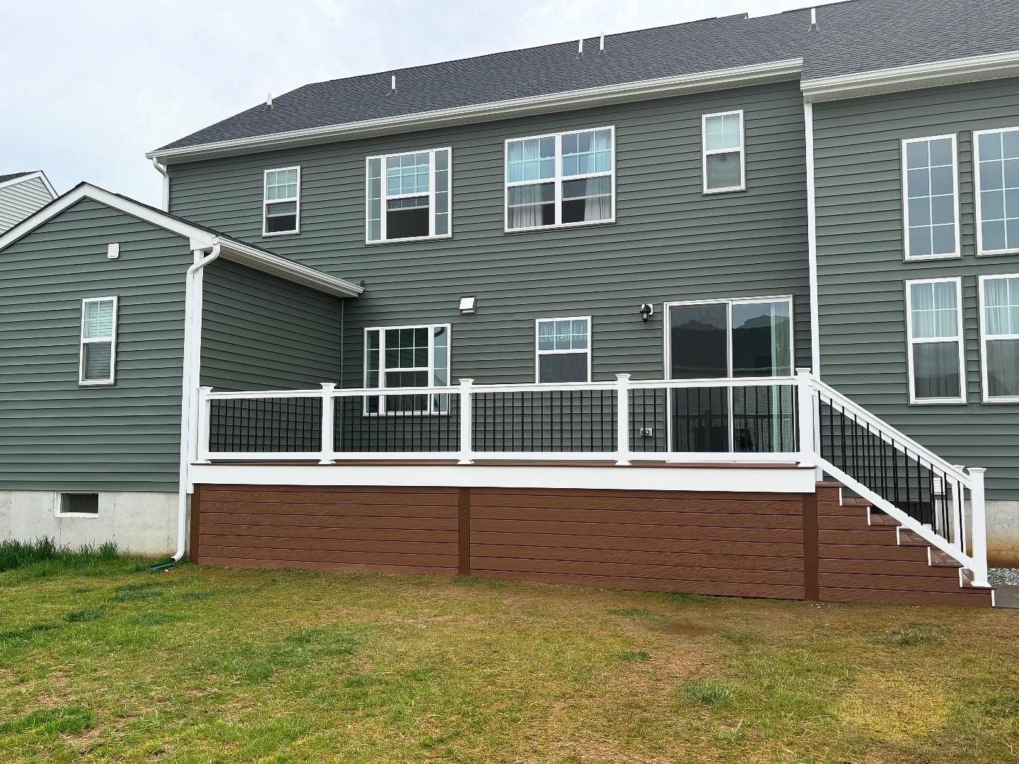 Back of a two-story green house with a deck and steps, set in a grassy yard.
