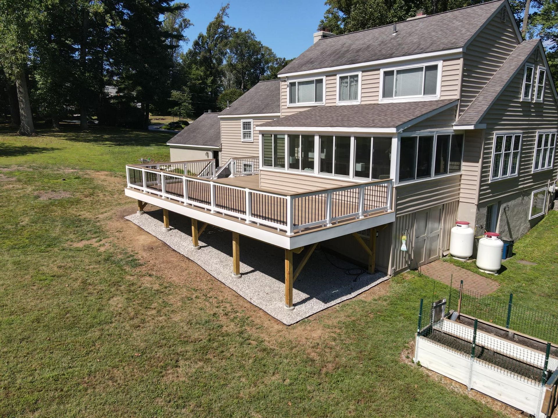 Large two-story house with a wooden deck. Deck has a screened-in porch area, gravel base, and propane tanks.