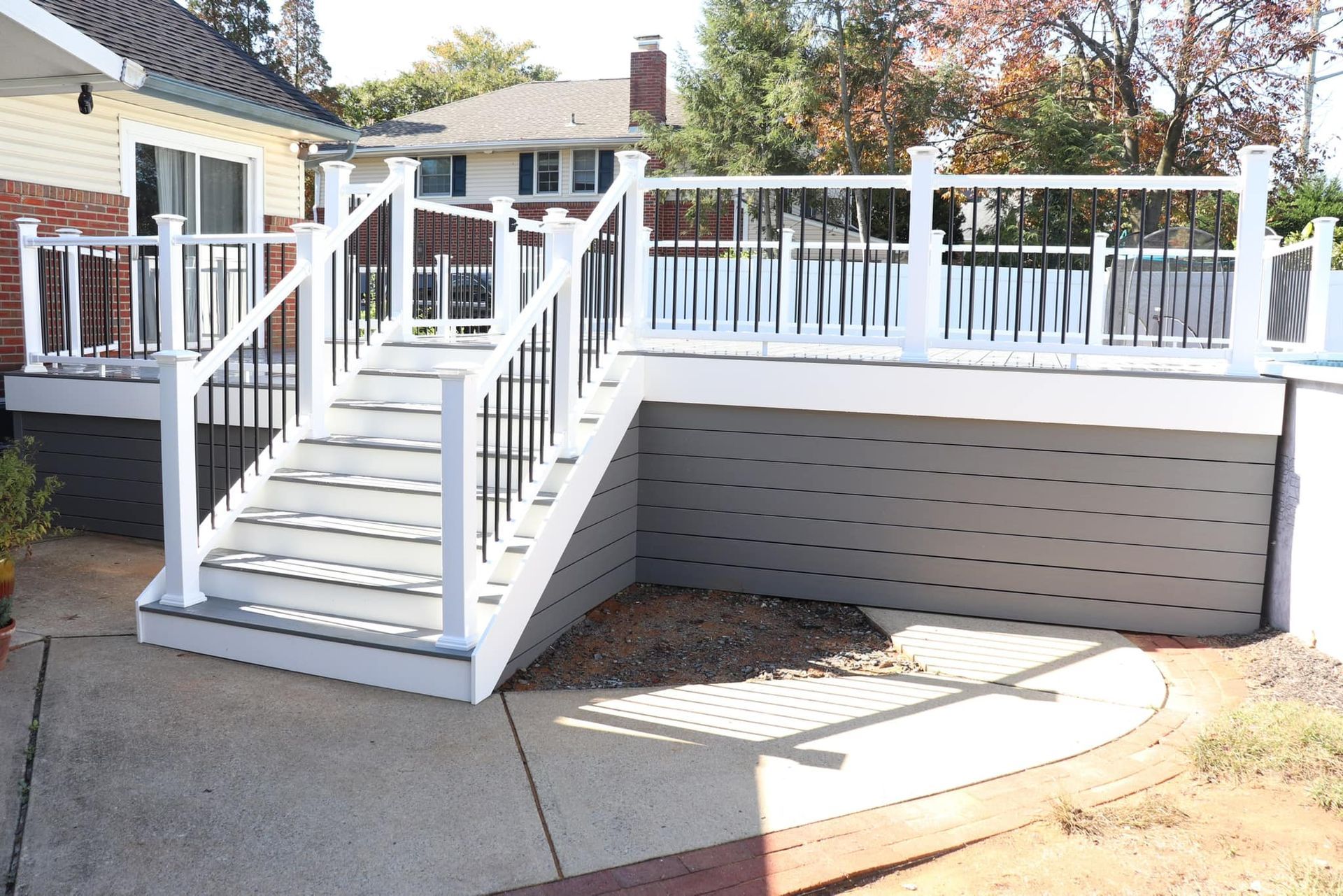 White and black deck with stairs, gray siding, concrete patio, and gravel area.