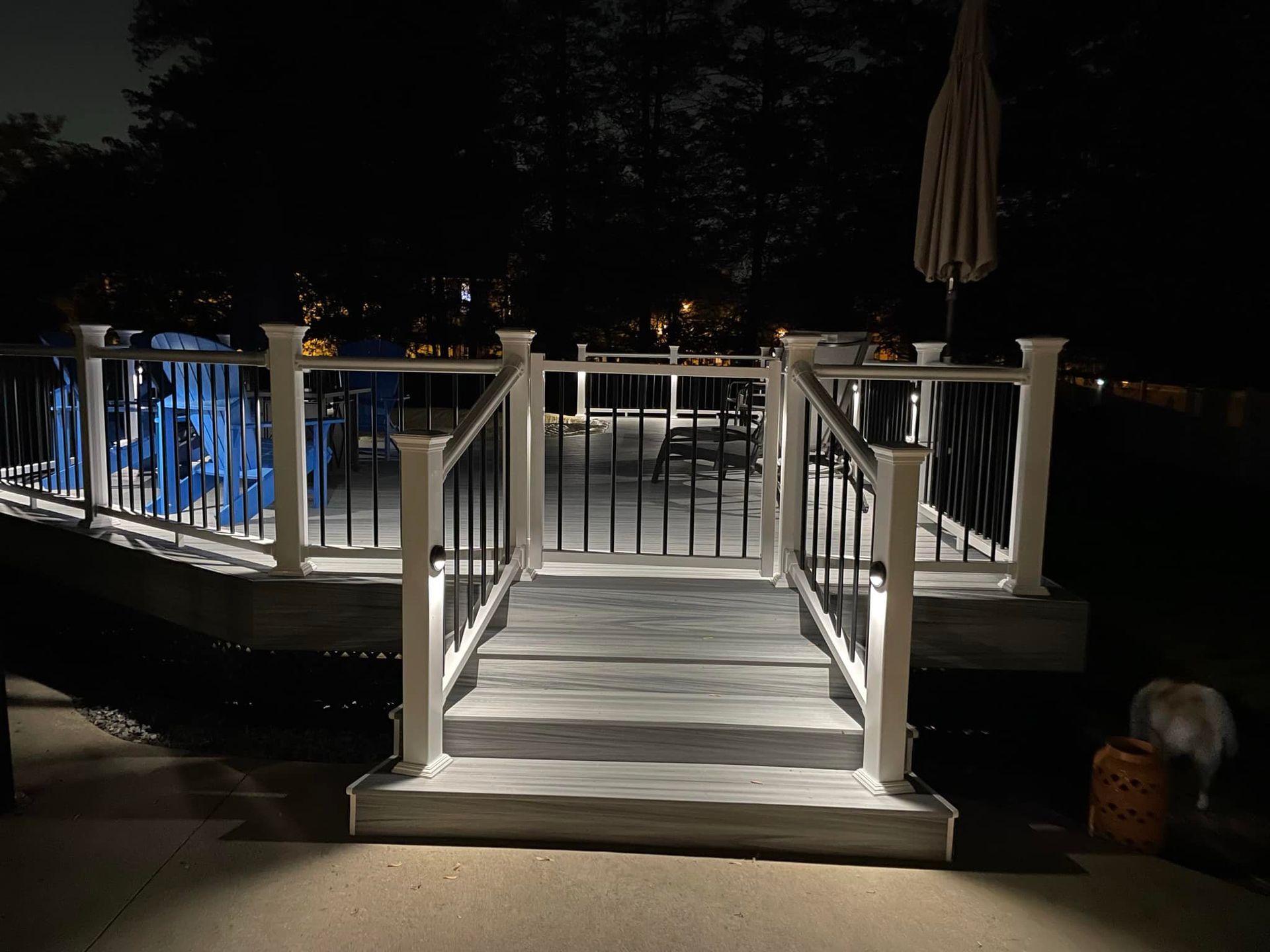 Lit deck at night with stairs, railing, and lights.