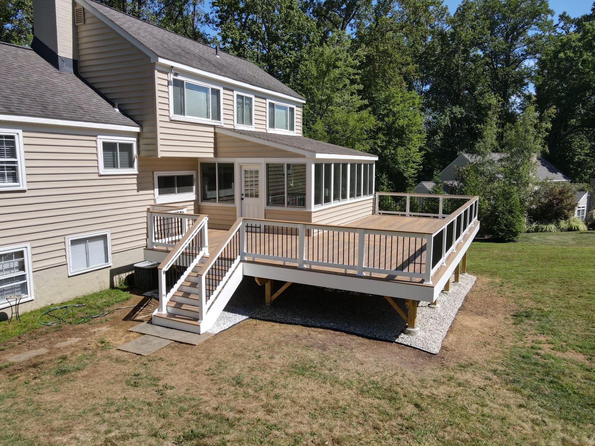 Two-story house with a large wooden deck and a screened-in porch on a grassy lawn.