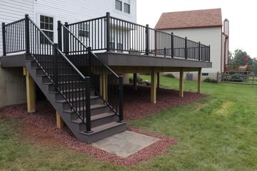 Black-railed deck with stairs, built against a white house and over a grassy yard. Red mulch borders the deck.