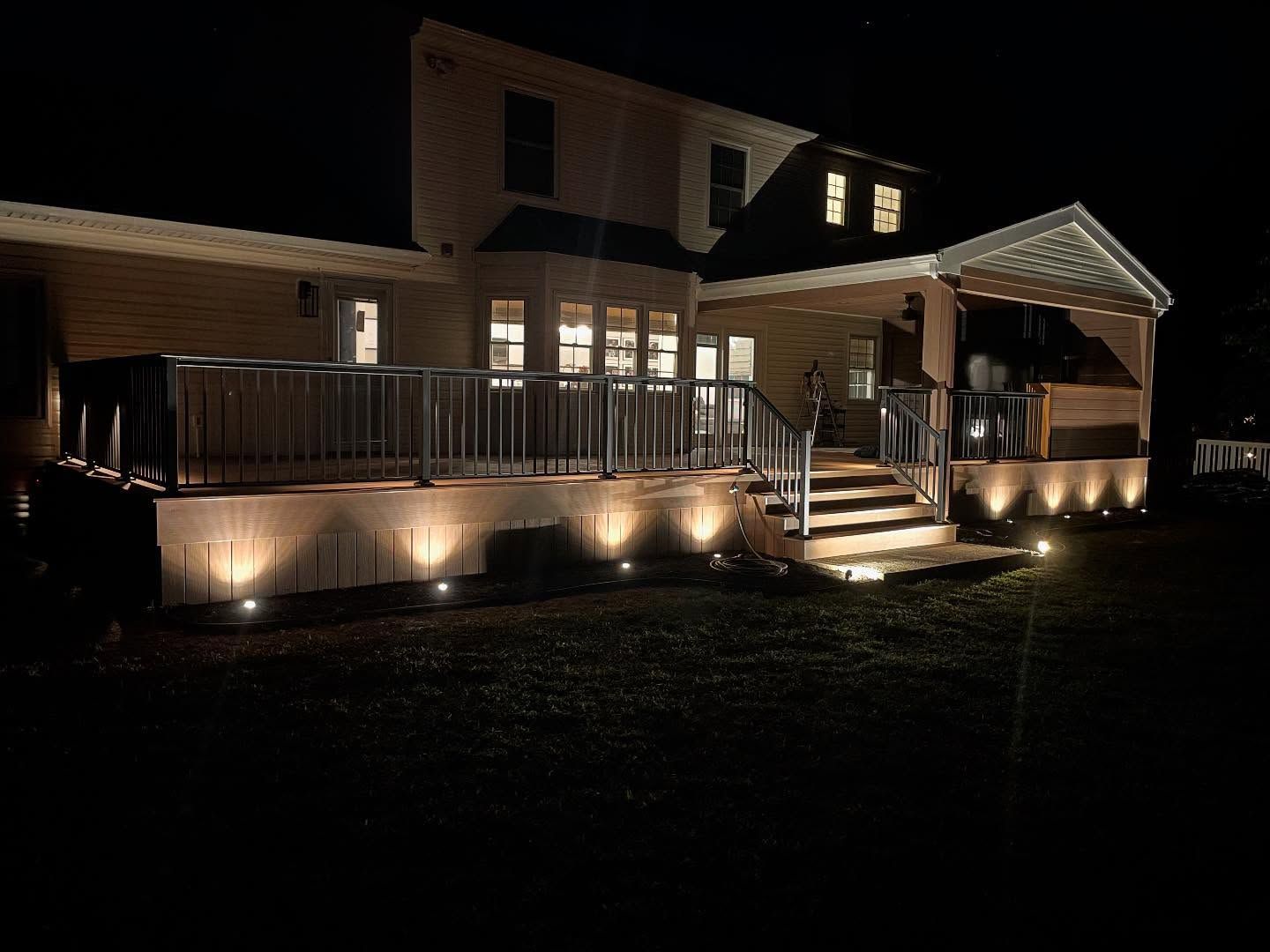 House exterior at night with deck and ground lights illuminating it.