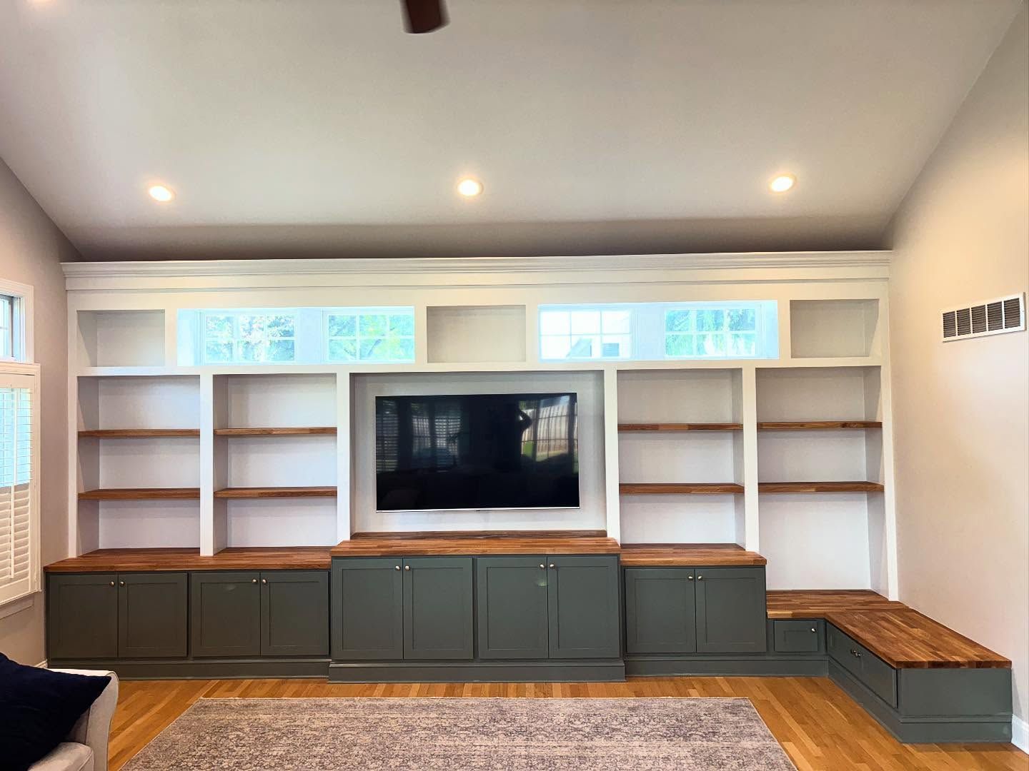 Built-in entertainment center with a TV, shelving, and lower cabinets. Green base cabinets, white shelving, and wood countertops.