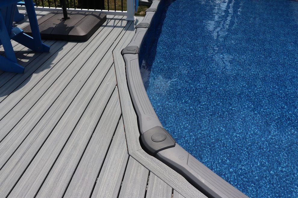 Deck with gray planks next to an above-ground pool filled with blue water.