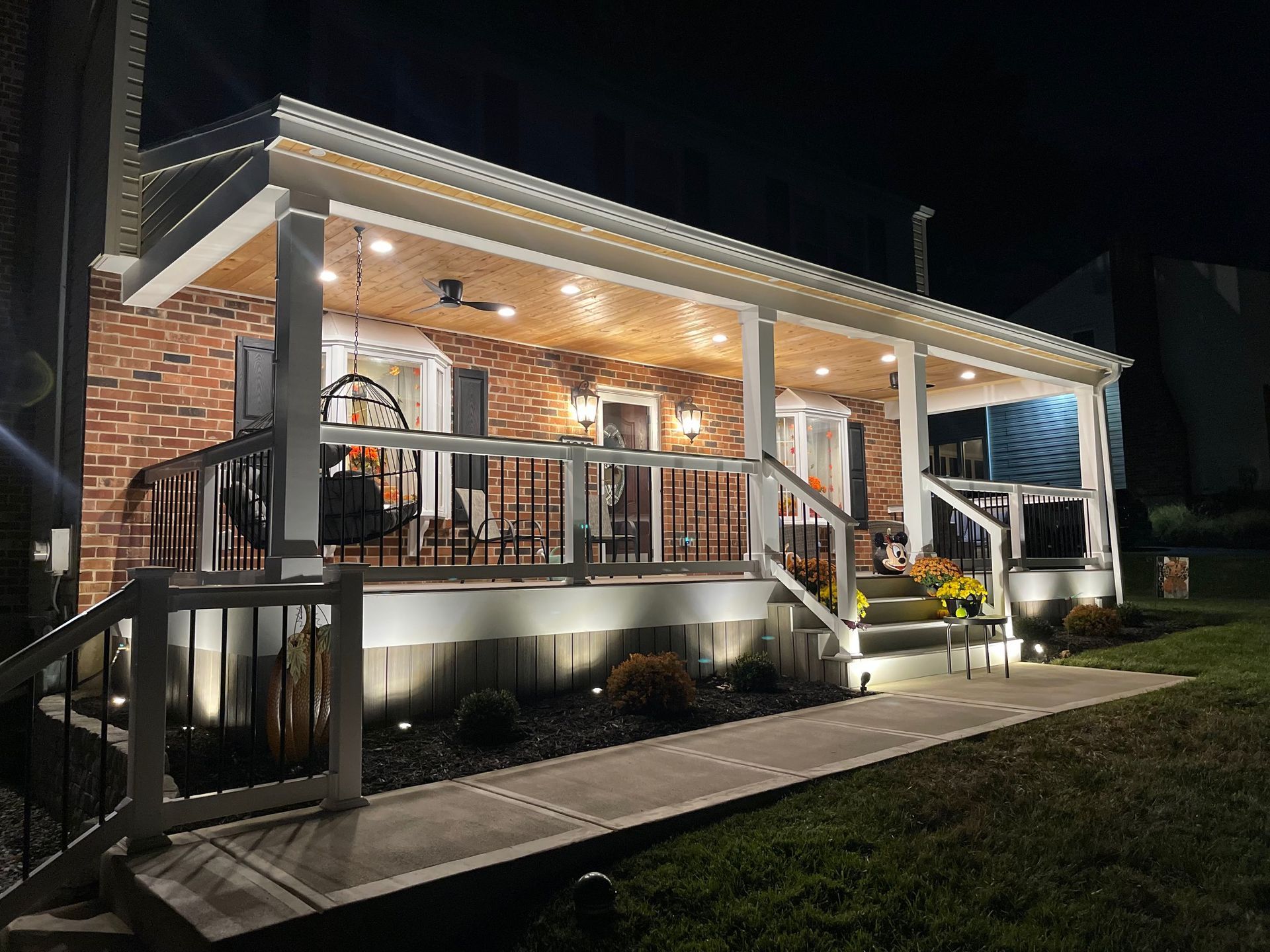 Lit up brick home porch at night with string lights, steps, and railing.