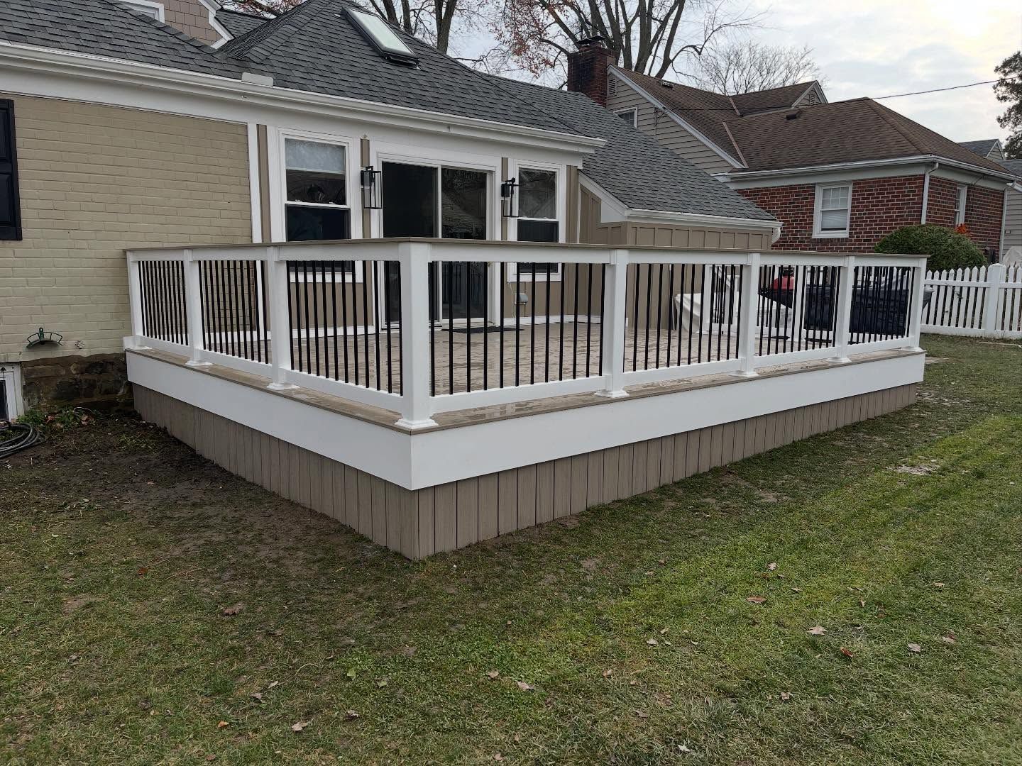 Backyard deck with white railing, brown base, attached to a house with sliding glass door.