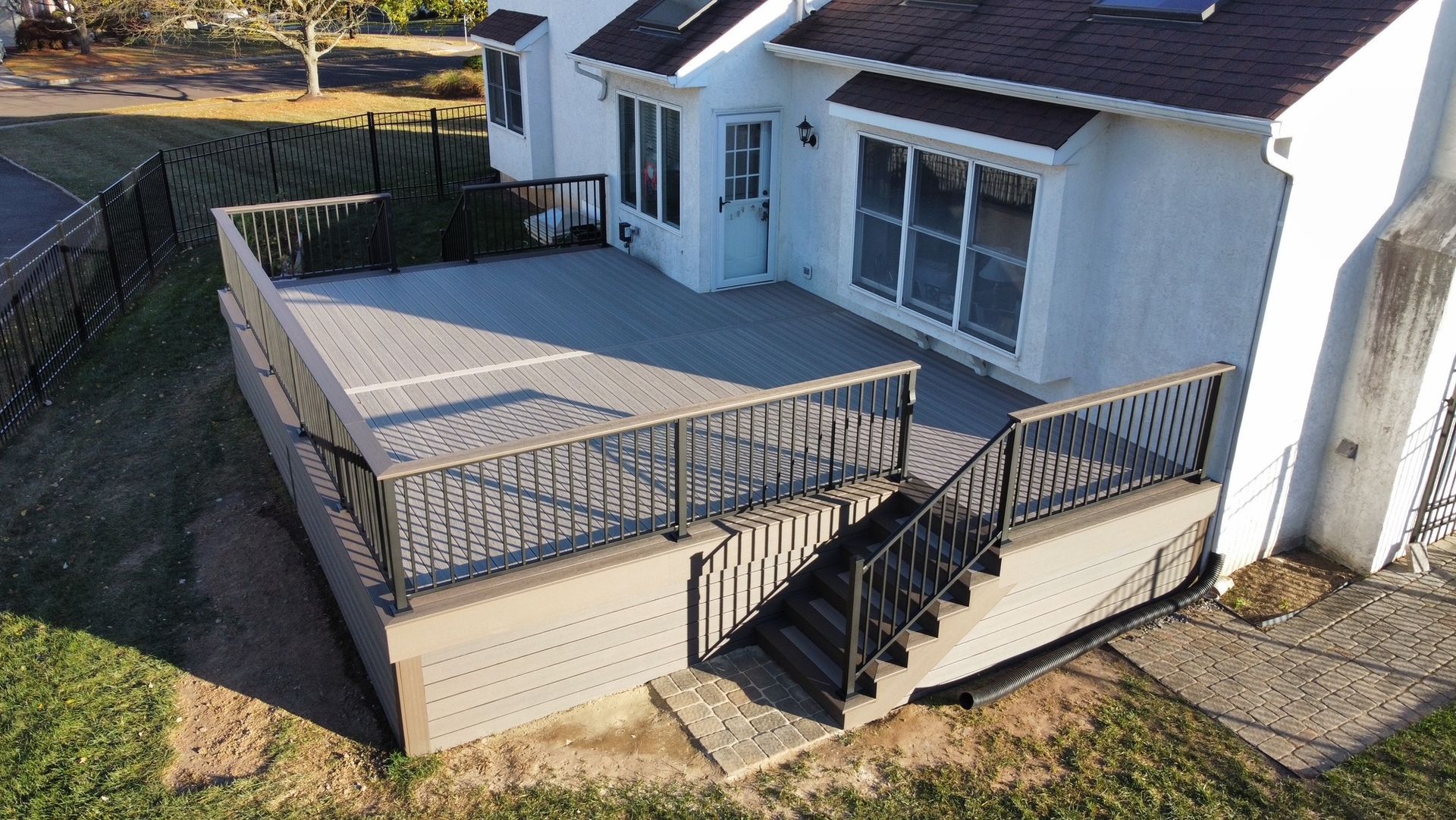 Elevated deck attached to a white house with stairs and black railing.