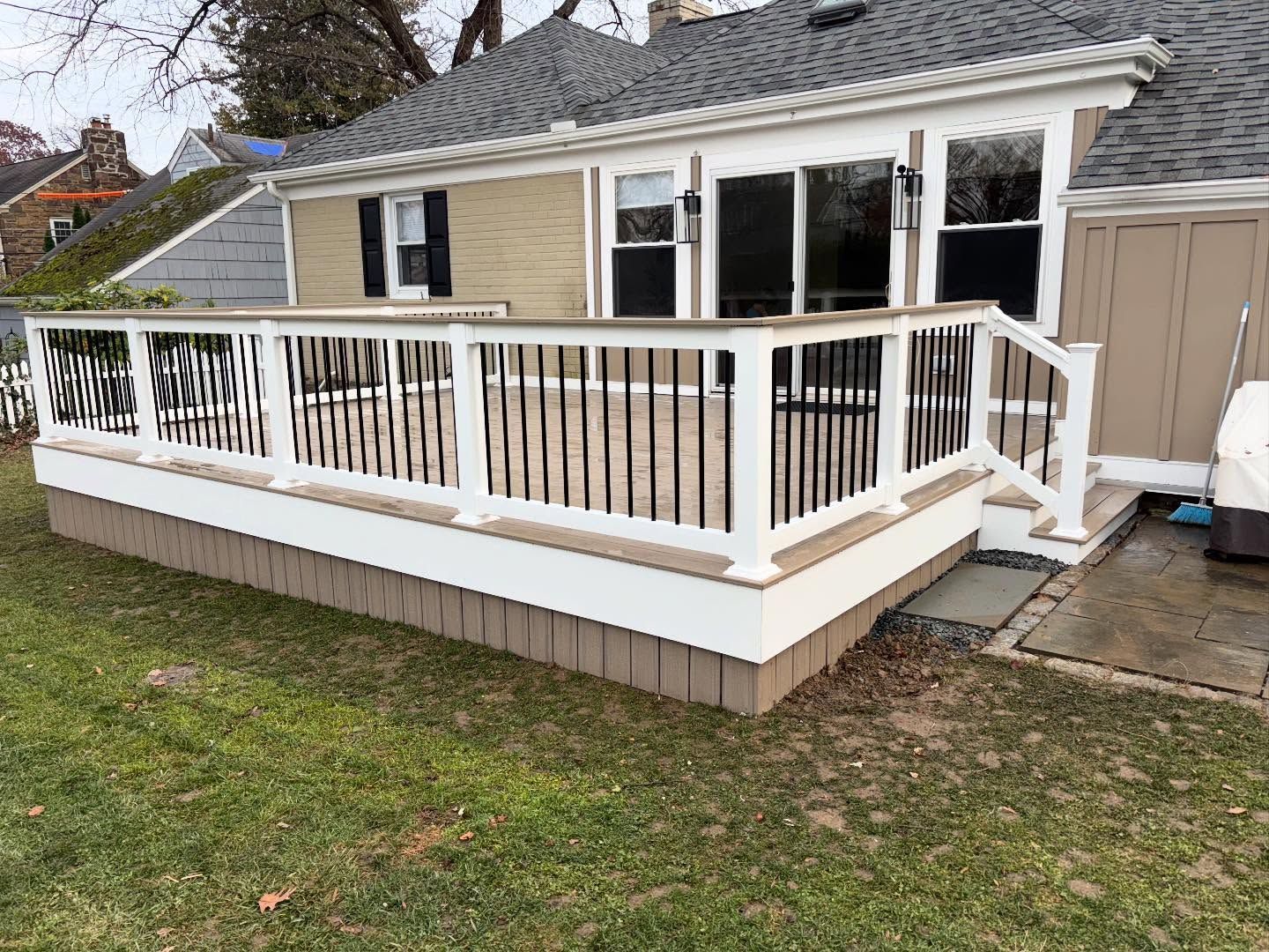 A deck attached to a house with white railing and black spindles, with a brown base and siding.