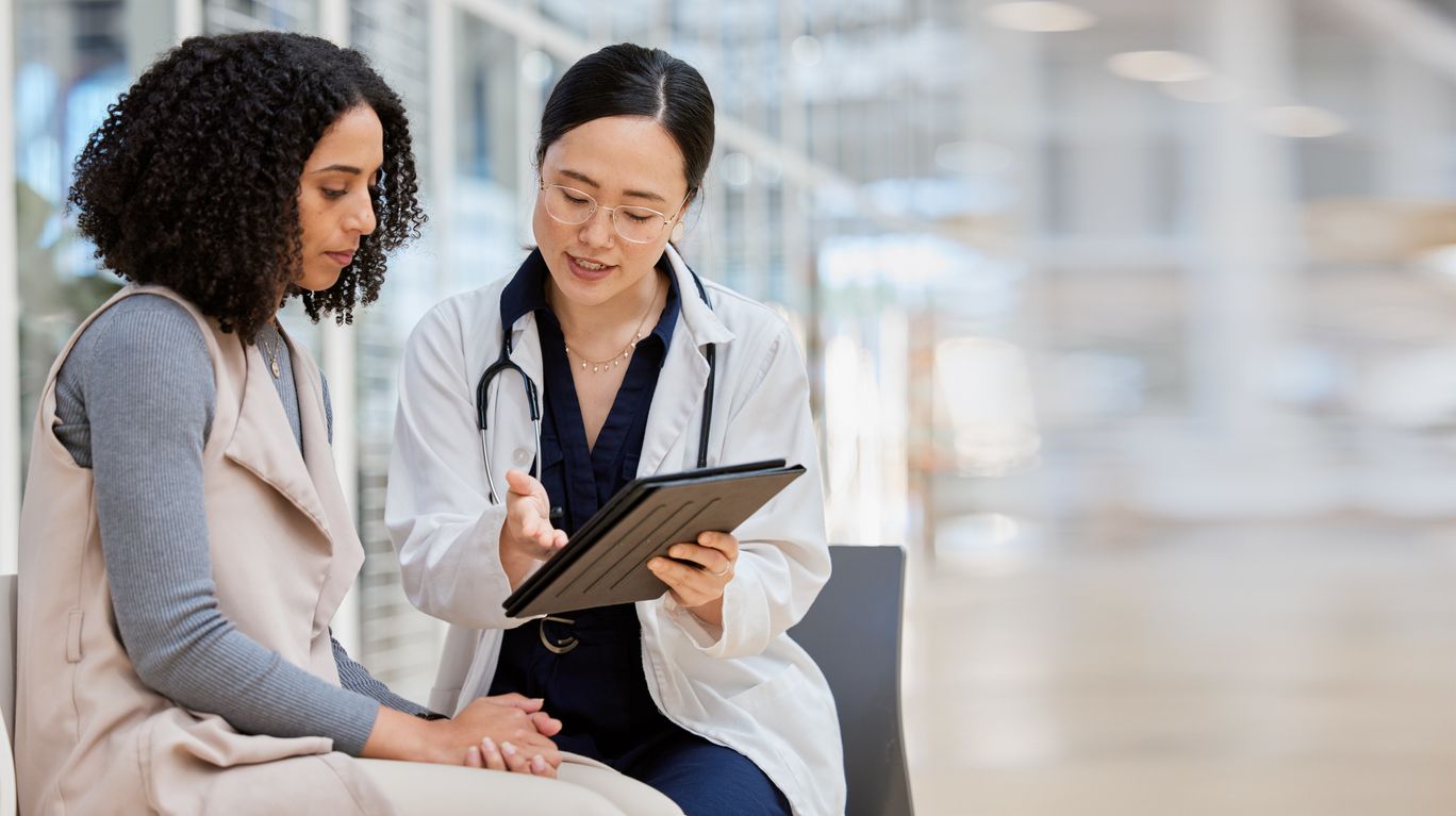 Doctor reviewing tablet with patient in a bright waiting area.