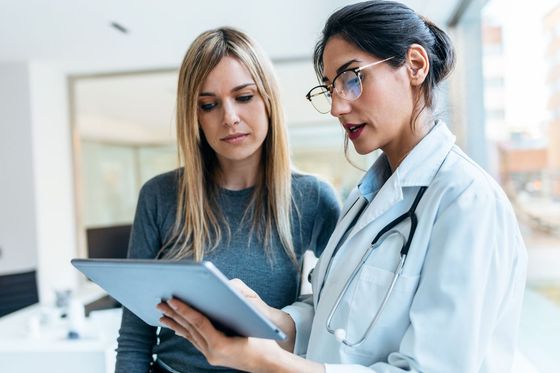 Doctor in white coat showing patient on tablet in office.