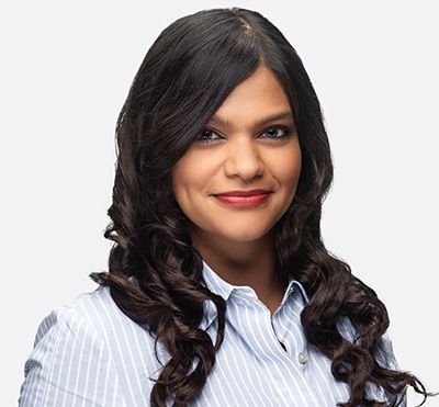 Woman with long, dark curly hair wearing a striped shirt smiles, looking at the camera.