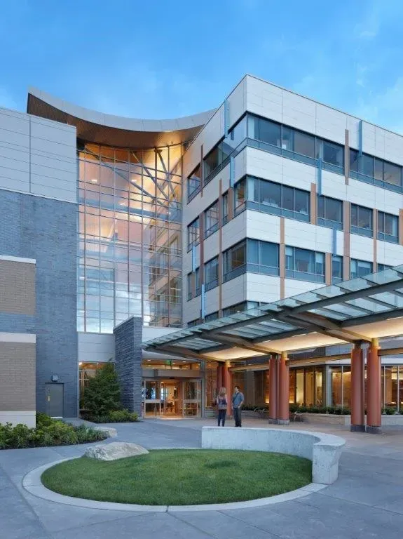 Modern hospital entrance with glass facade, covered drop-off area, and a small circular lawn.