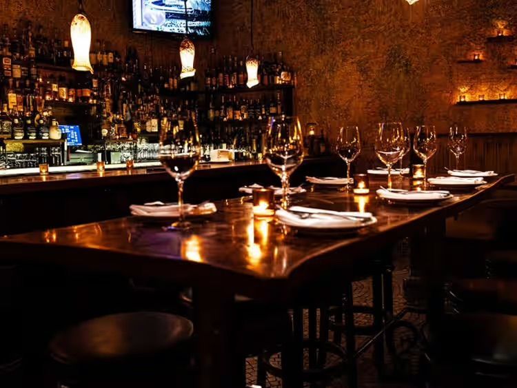 Dimly lit bar with set wine glasses and plates on a polished wooden table