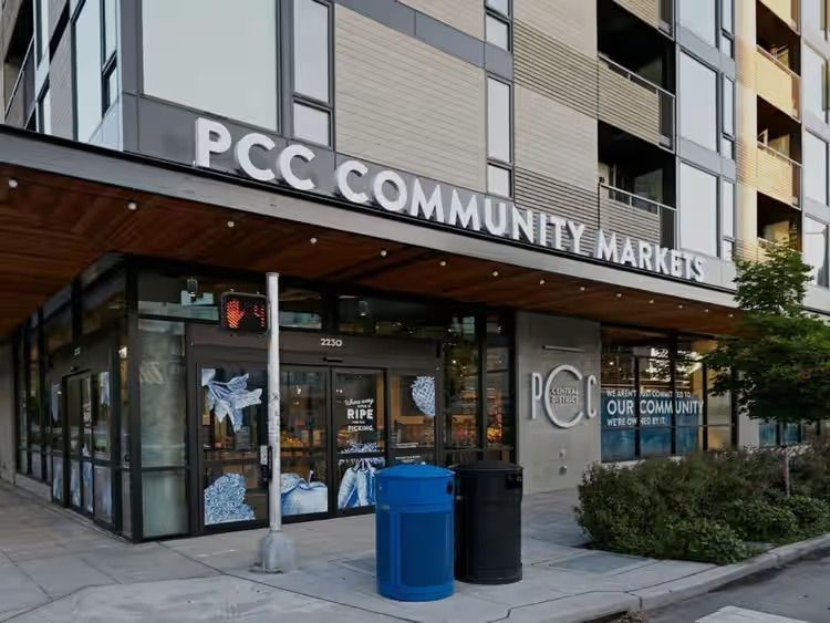 PCC Community Markets storefront with glass entrance and blue recycling bin outside