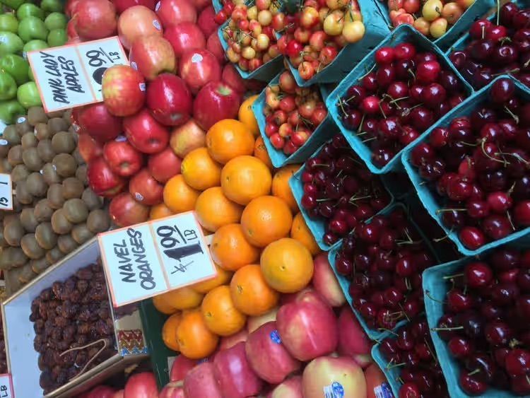 Assorted fresh fruit at a market, including cherries, apricots, apples, kiwis, and grapes in baskets.