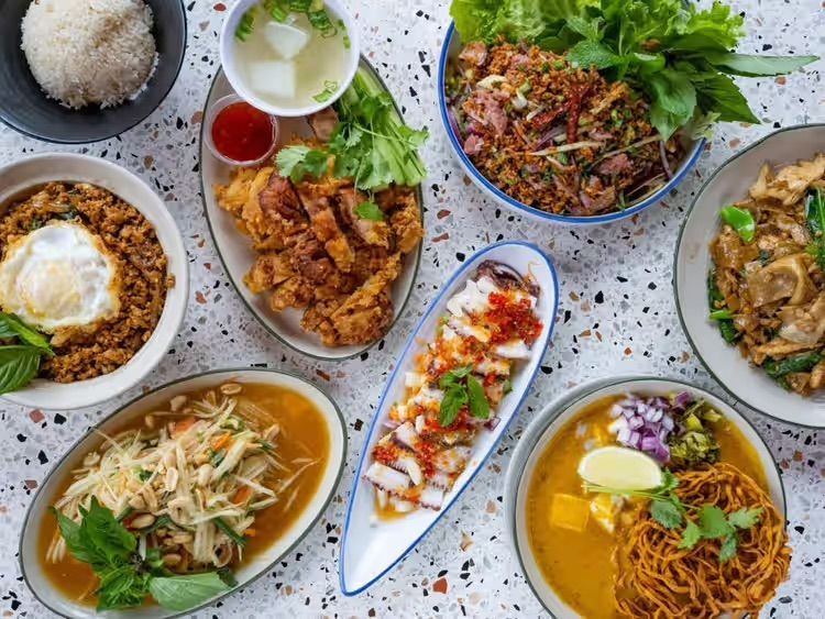 Assorted Asian dishes arranged on a table, including noodles, rice, soup, and stir-fried meats.