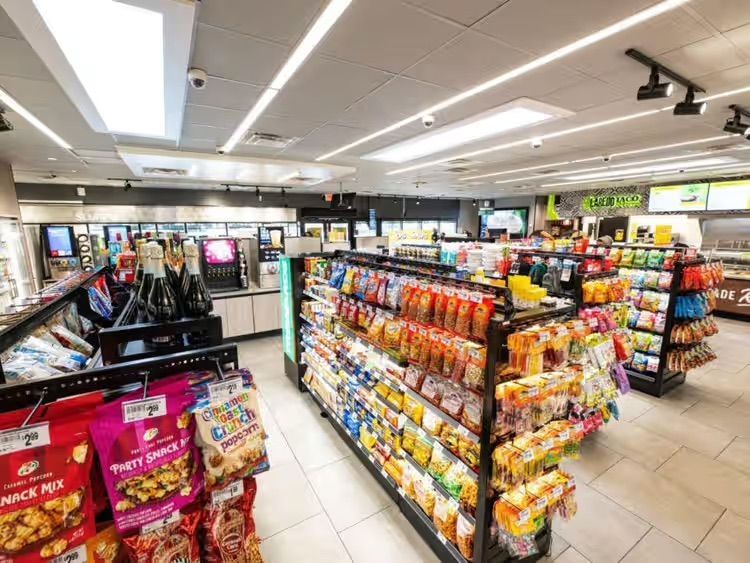 Convenience store interior with aisles of snacks, drinks, and checkout counters under bright lighting