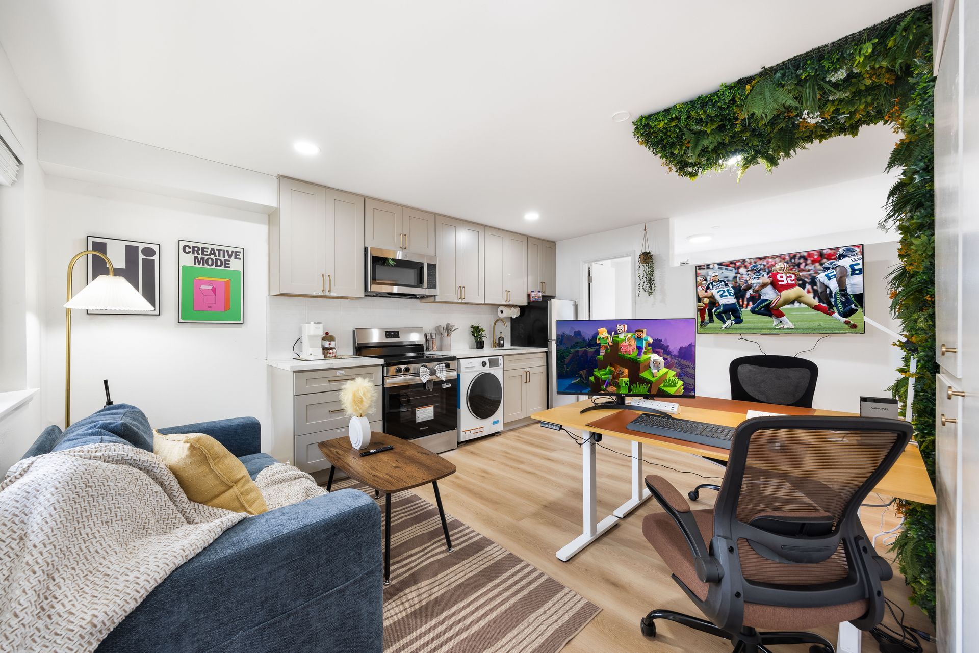 Modern living room with sofa, desk, TV, and open kitchen in bright white decor.