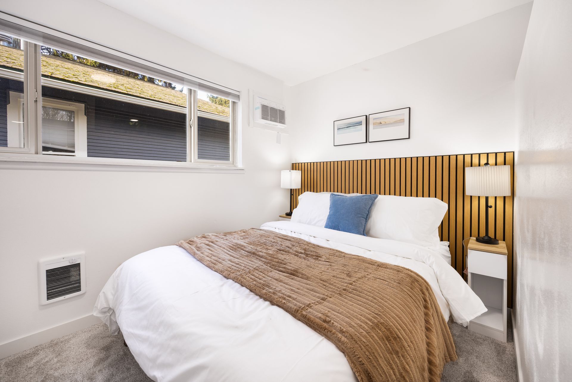 Bright modern bedroom with white bedding, wood headboard, blue pillow, and window light