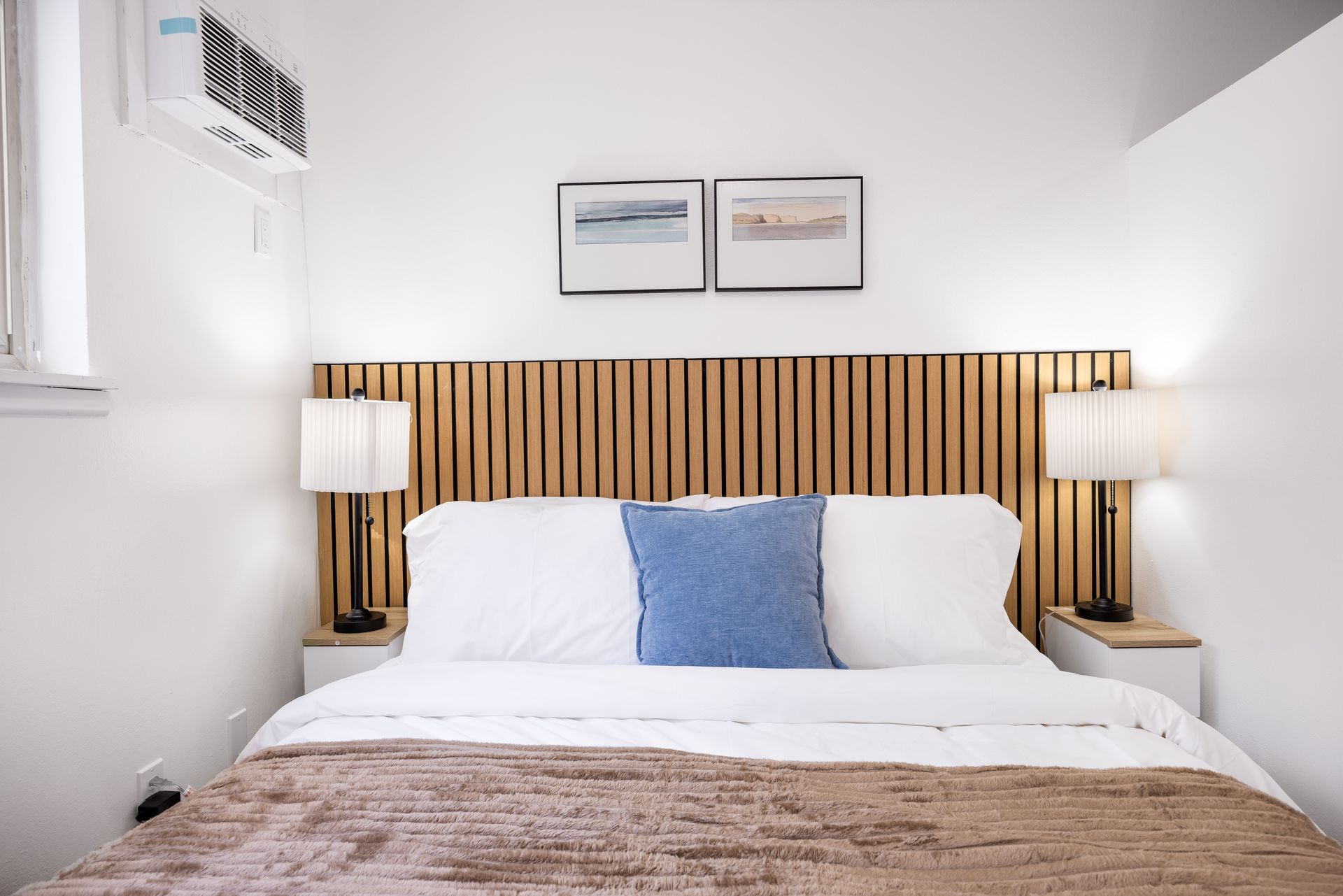 Bright minimalist bedroom with white bedding, blue accent pillow, wooden headboard, and bedside lamps