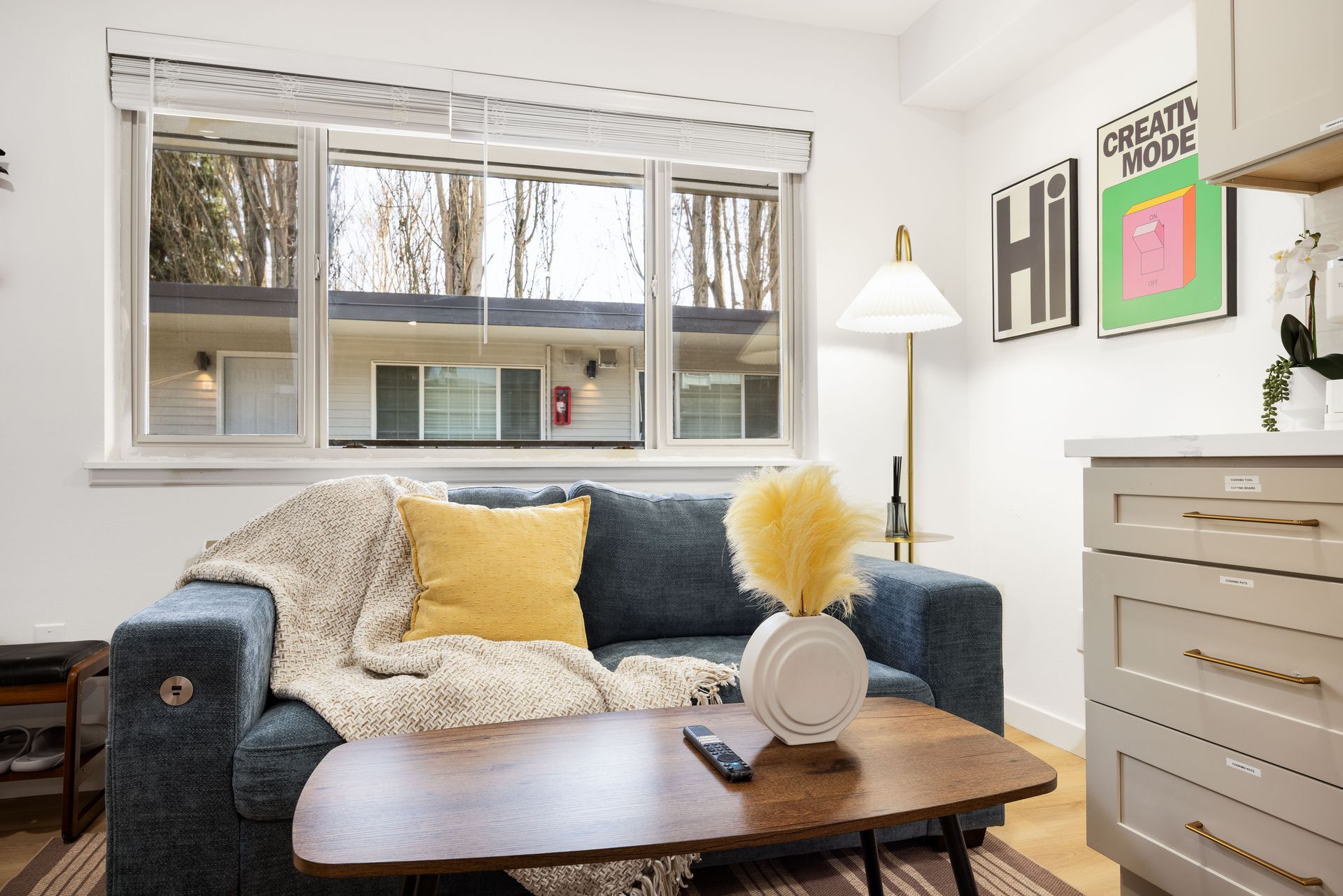 Cozy living room with navy sofa, yellow pillows, coffee table, floor lamp, and dresser by bright windows