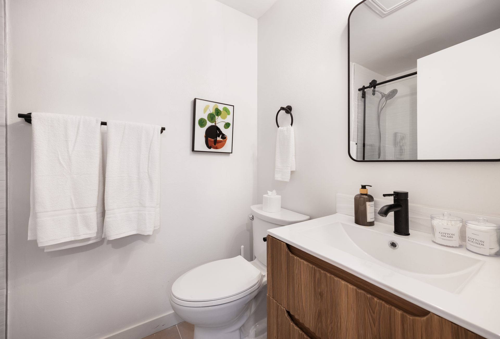 Minimal white bathroom with wood vanity, toilet, towel rack, and mirror above the sink.