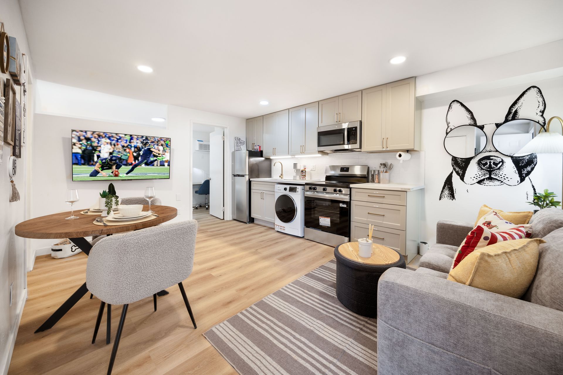 Bright open-plan living room and kitchen with sofa, round table, striped rug, and butterfly wall art