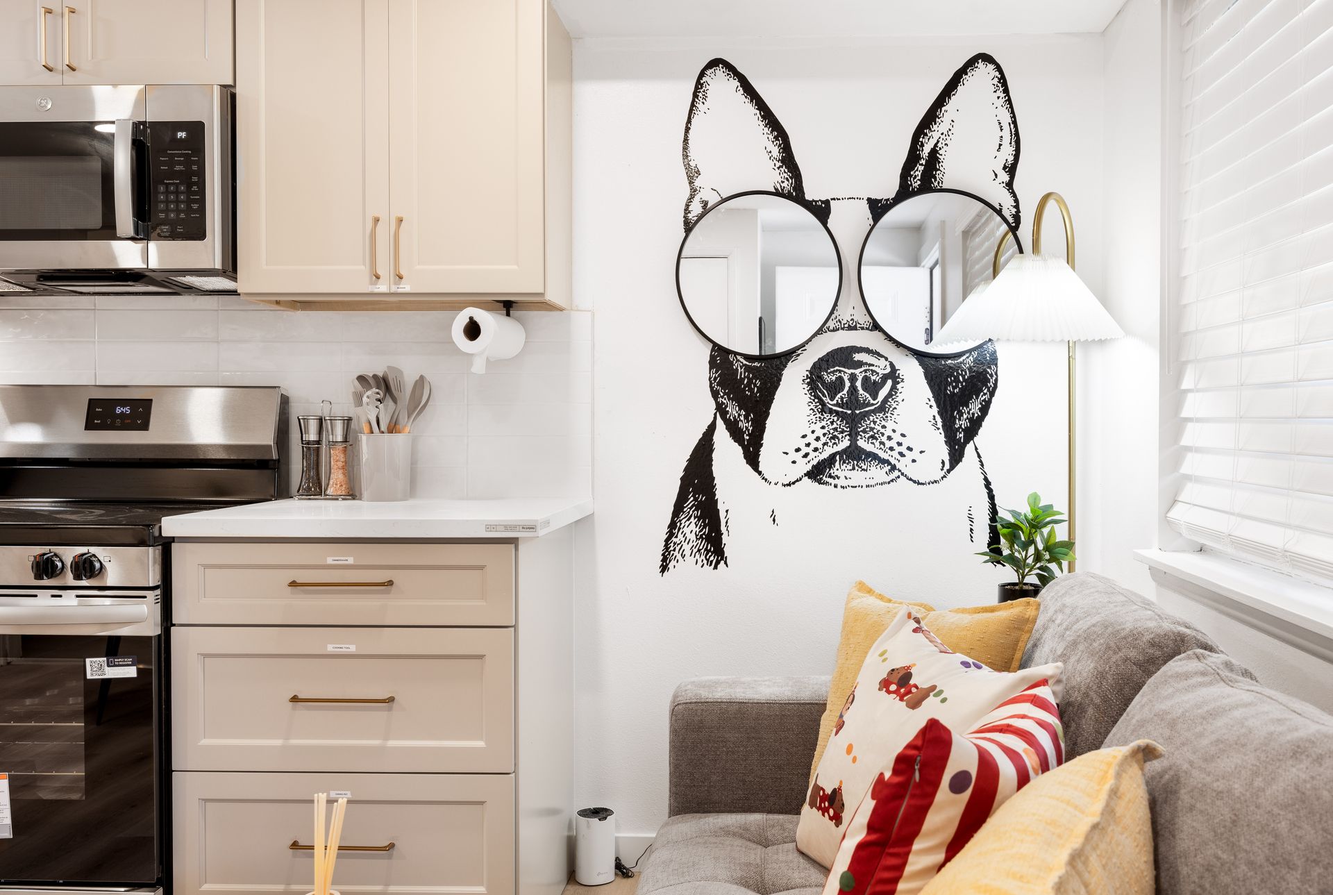 Kitchen with beige cabinets and stainless appliances, plus a sofa and dog mural on the wall.