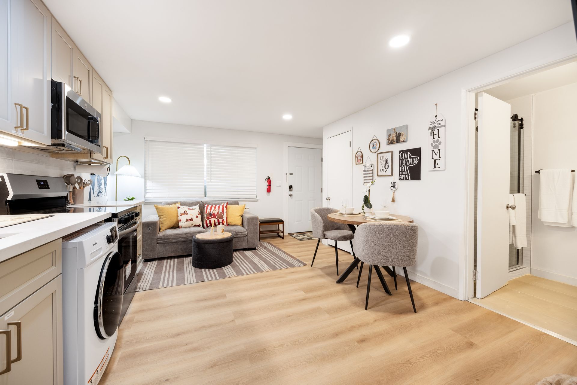 Bright open-plan apartment with kitchen, dining table, sofa, and wall art on light wood flooring