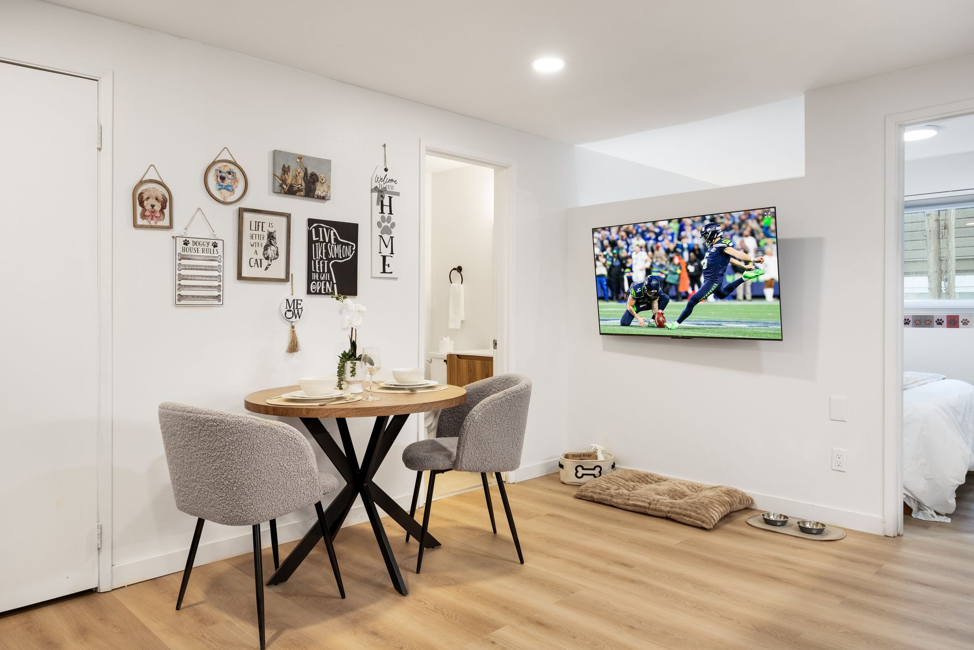 Bright dining nook with round table, gray chairs, wall art, and a TV in a modern white living room.