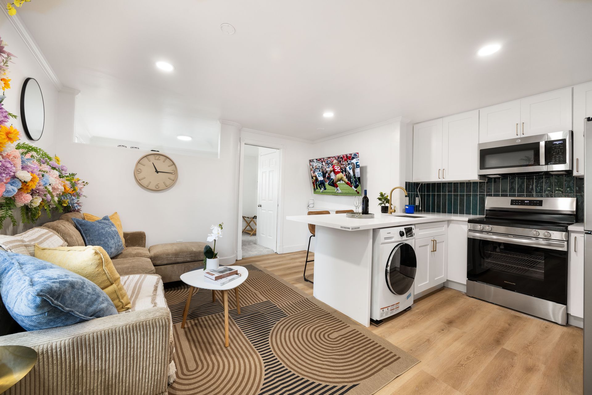 Bright modern living room and kitchen with white cabinets, patterned rug, sofa, and wall art