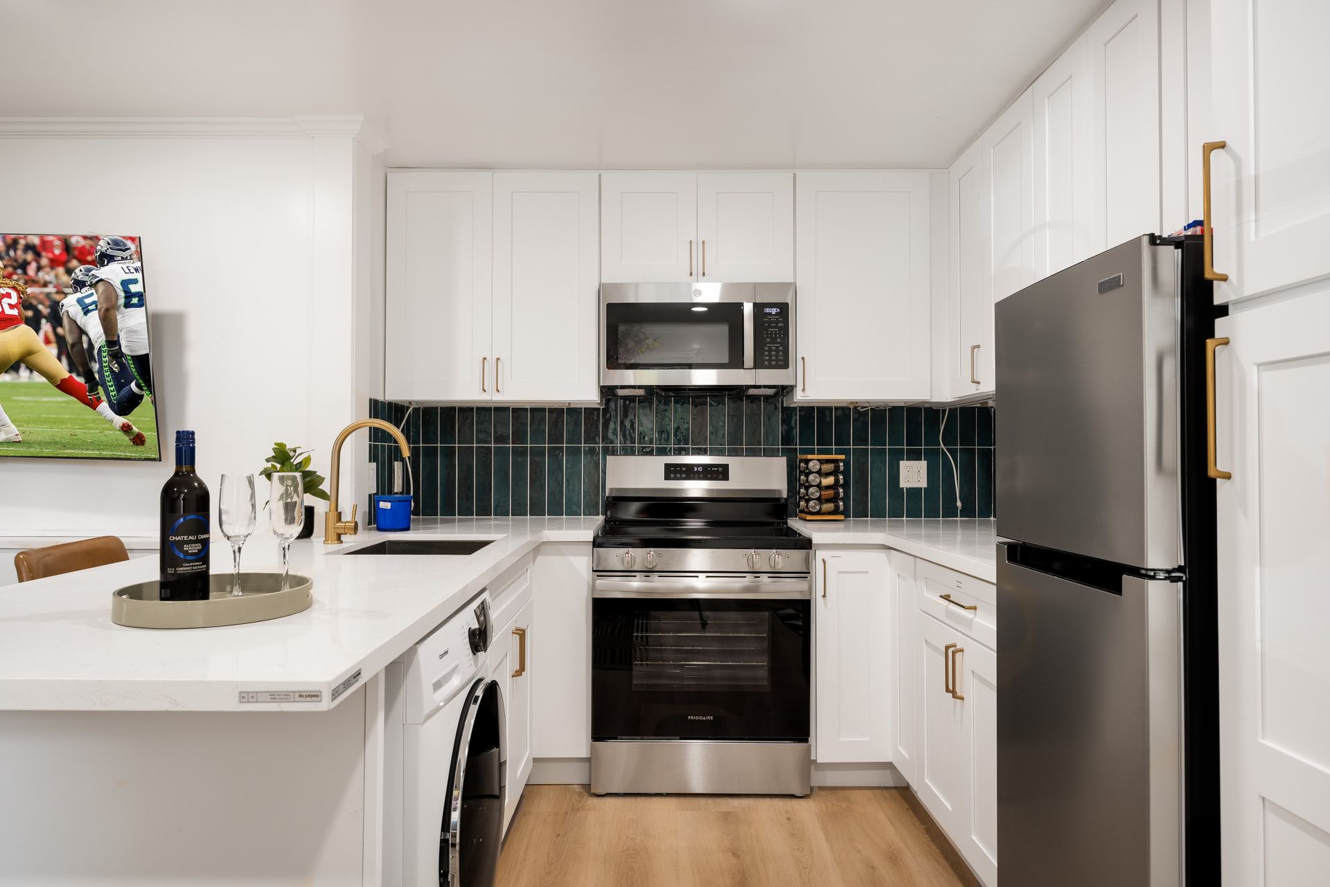 Modern white kitchen with stainless steel appliances, dark tile backsplash, and light wood floor