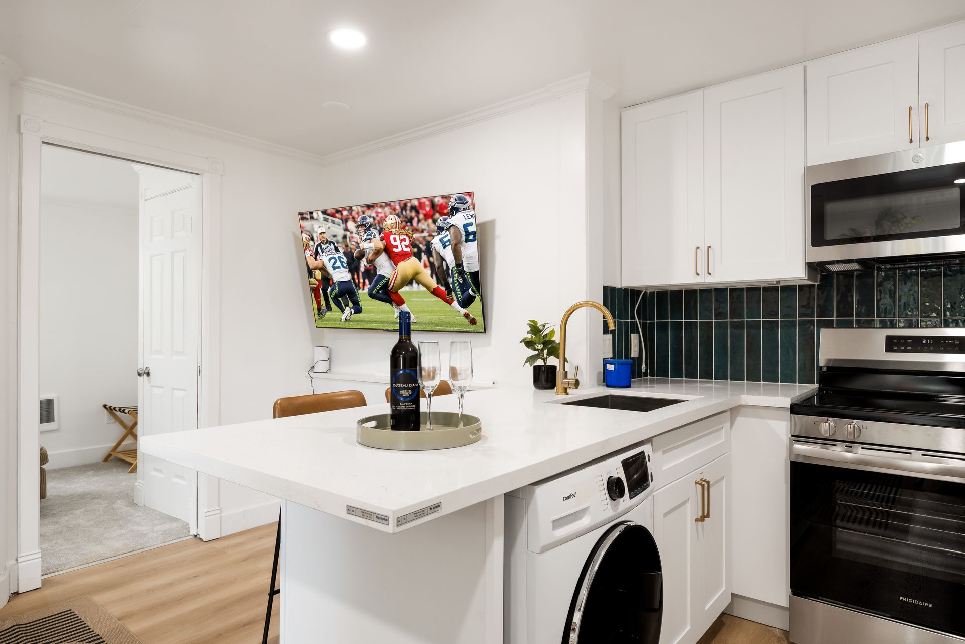 Bright modern kitchen with island, wine bottle, TV, and black appliances