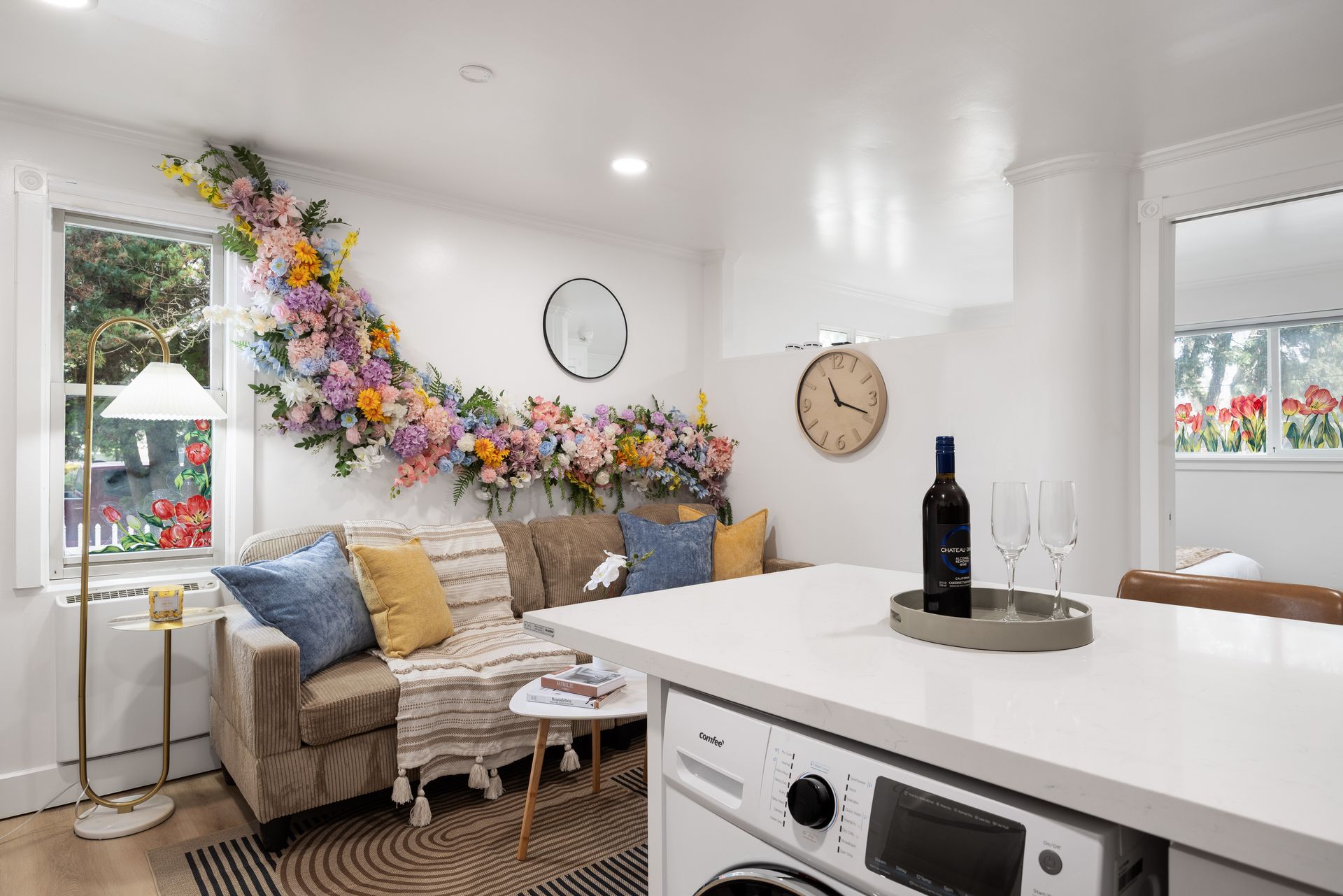 Bright living room with floral wall decor, beige sofa, white table, and washer in foreground