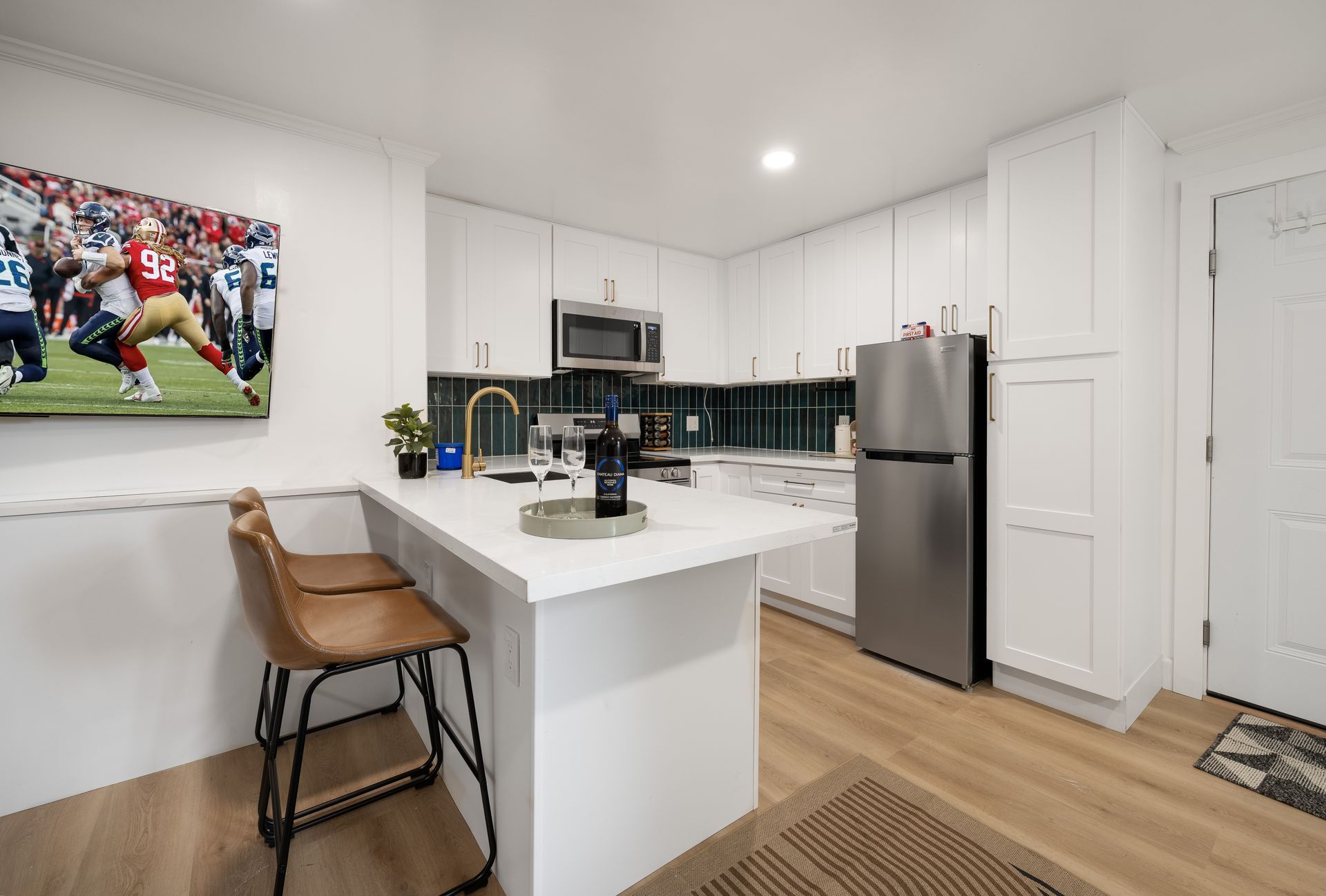 Modern kitchen with white cabinets, stainless fridge, island seating, and football artwork on the wall