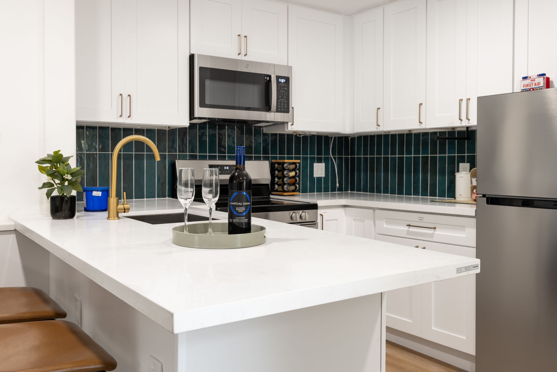 Modern white kitchen with island, dark tile backsplash, stainless appliances, and a potted plant by the sink
